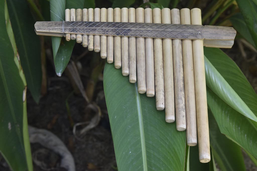 Close-up of a bamboo pan flute resting on vibrant green leaves, showcasing traditional craftsmanship.